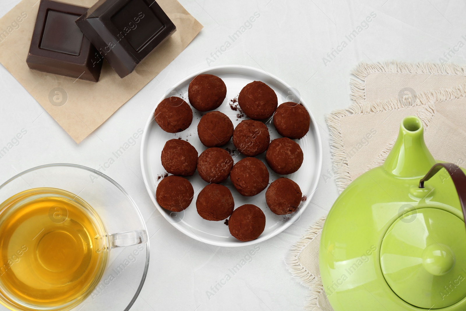 Photo of Delicious chocolate candies powdered with cocoa and tea on white table, flat lay