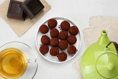 Delicious chocolate candies powdered with cocoa and tea on white table, flat lay