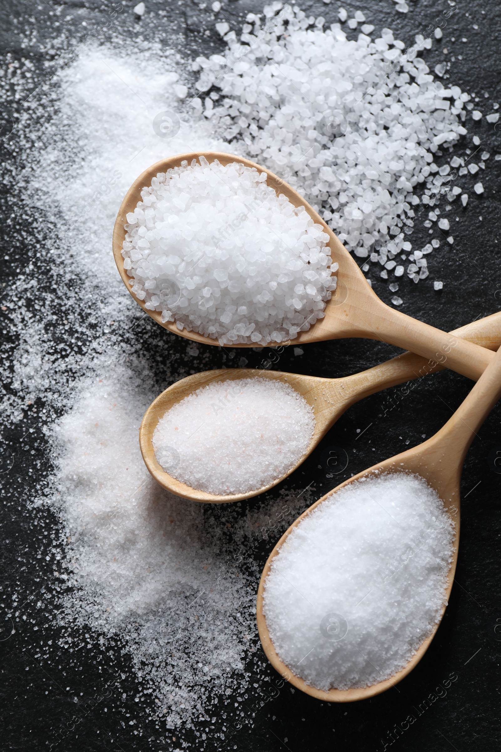 Photo of Organic salt in spoons on black table, flat lay