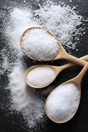 Photo of Organic salt in spoons on black table, flat lay