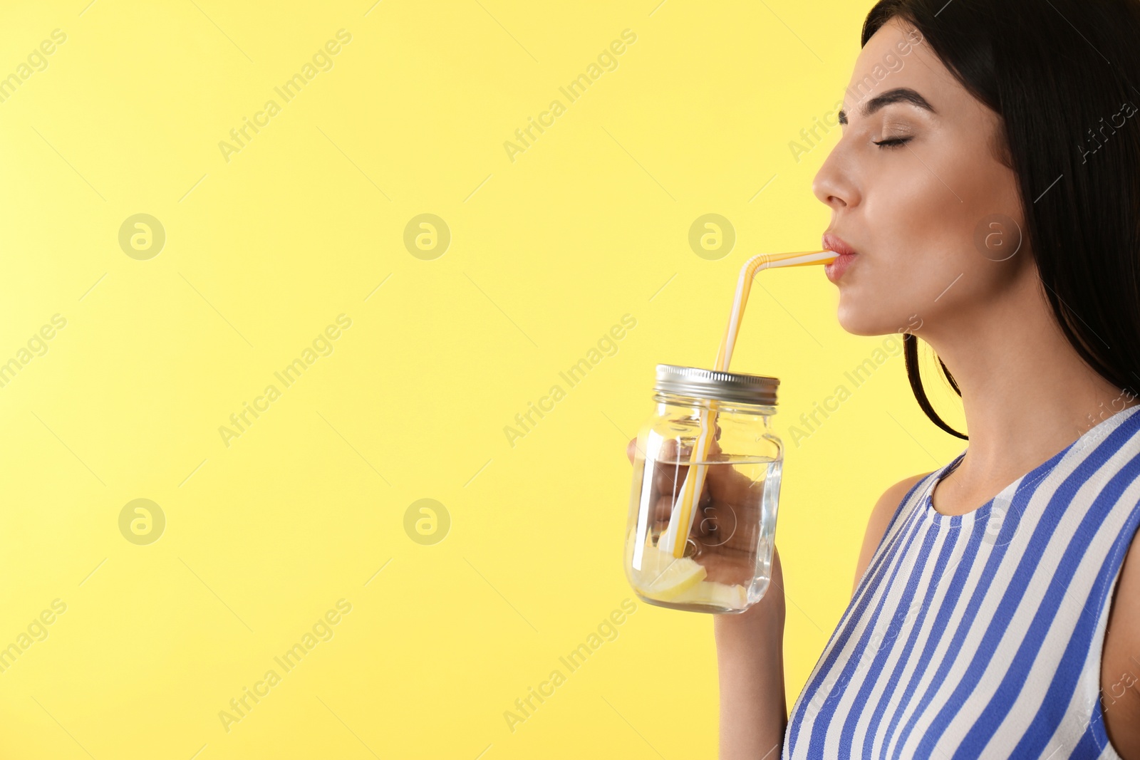 Photo of Beautiful young woman drinking tasty lemon water on yellow background, closeup. Space for text