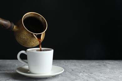 Photo of Turkish coffee. Pouring brewed beverage from cezve into cup at grey table. Space for text