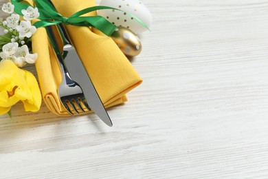 Photo of Cutlery set, Easter eggs and beautiful flowers on white wooden table, space for text