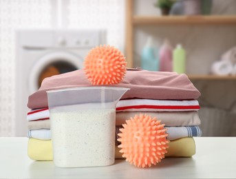 Dryer balls, detergent and stacked clean clothes on marble table in laundry room