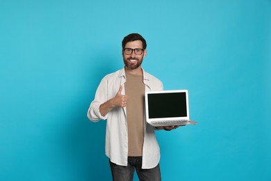 Photo of Handsome man with laptop showing thumb up gesture on light blue background