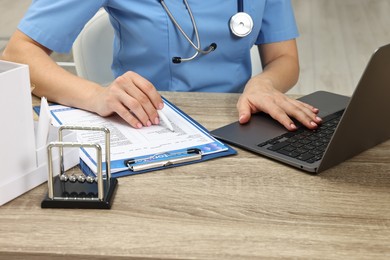 Doctor working with results of laboratory test and laptop at wooden table in clinic, closeup