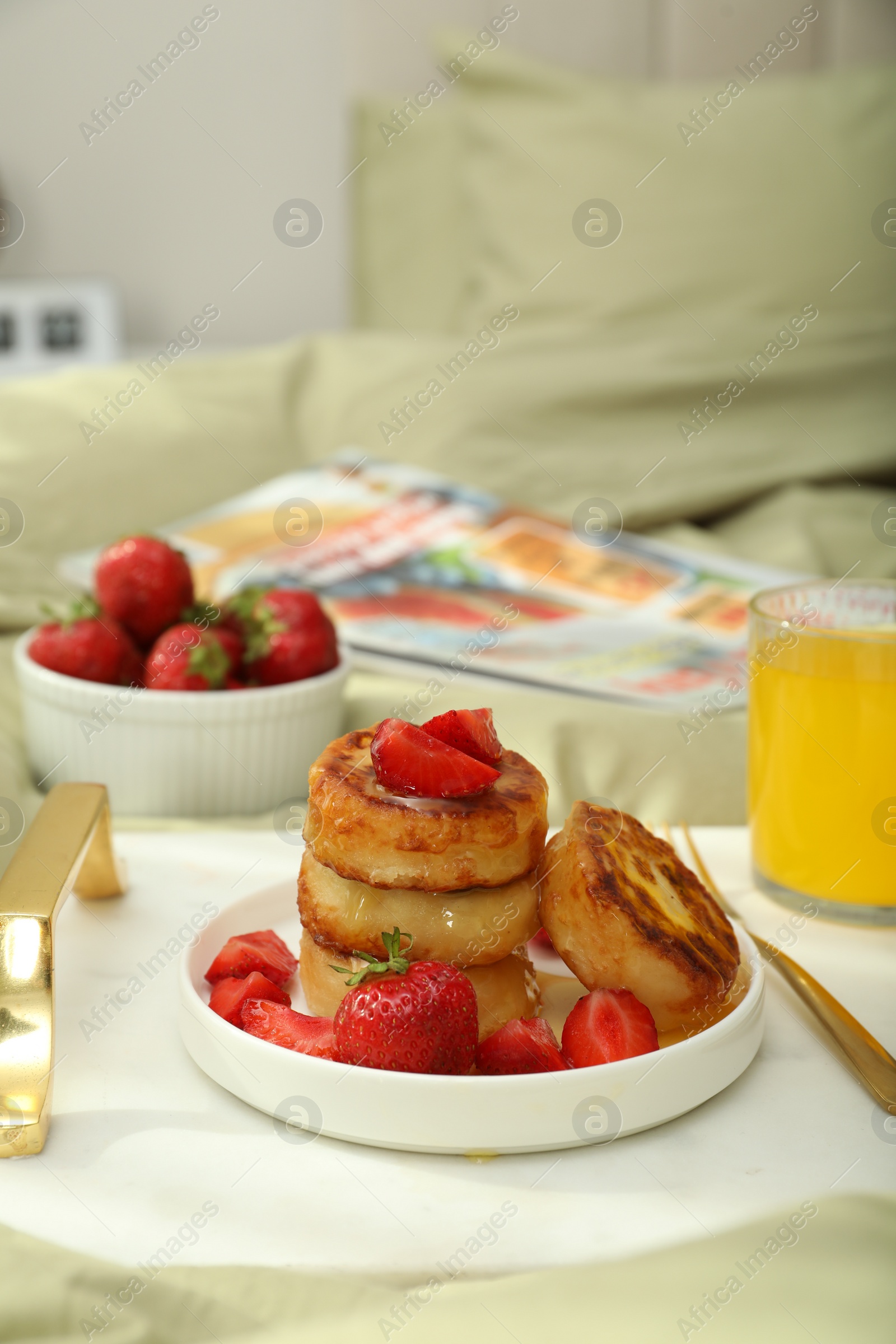 Photo of Tasty breakfast served in bedroom. Cottage cheese pancakes with strawberries and honey on white tray