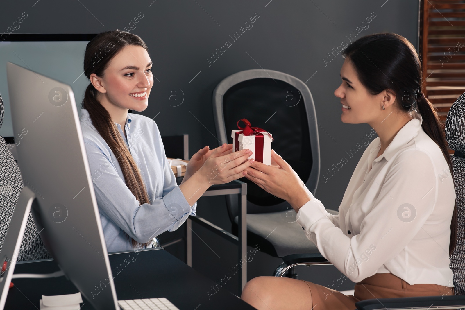 Photo of Woman presenting gift to her colleague in office