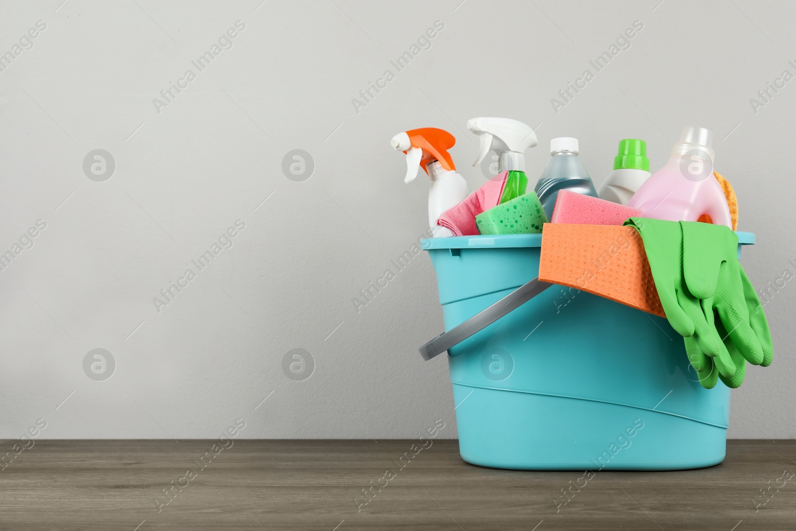 Photo of Light blue bucket with cleaning products on wooden table. Space for text