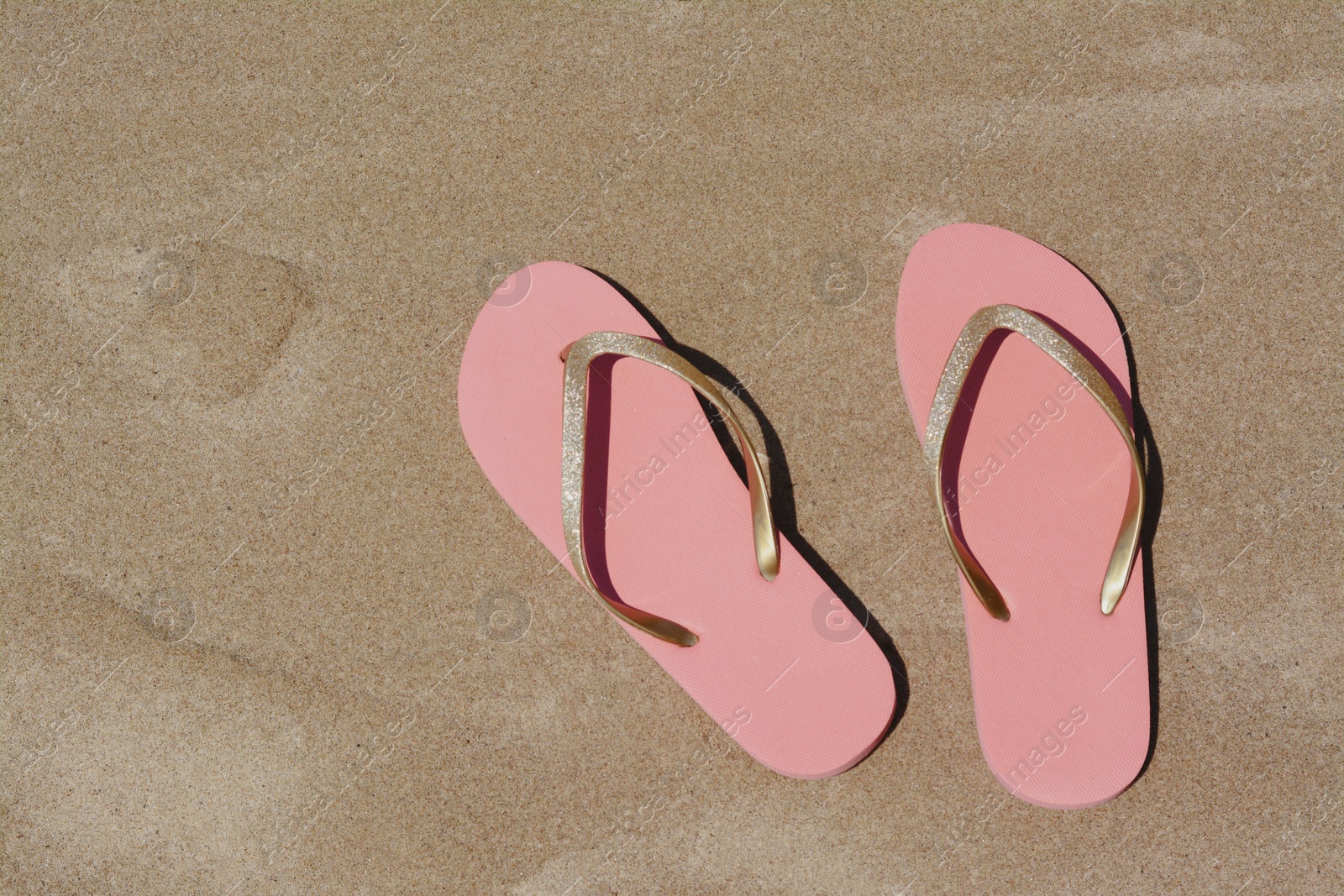 Photo of Stylish pink flip flops on wet sand, flat lay