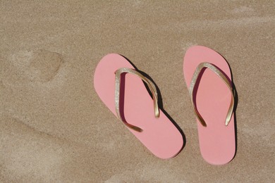 Photo of Stylish pink flip flops on wet sand, flat lay