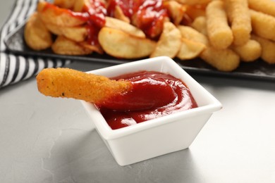 Photo of Delicious cheese stick and ketchup in bowl on light grey table, closeup