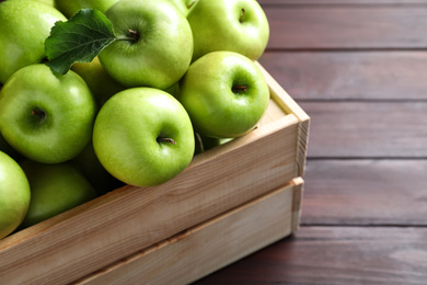 Juicy green apples in crate on wooden table, closeup