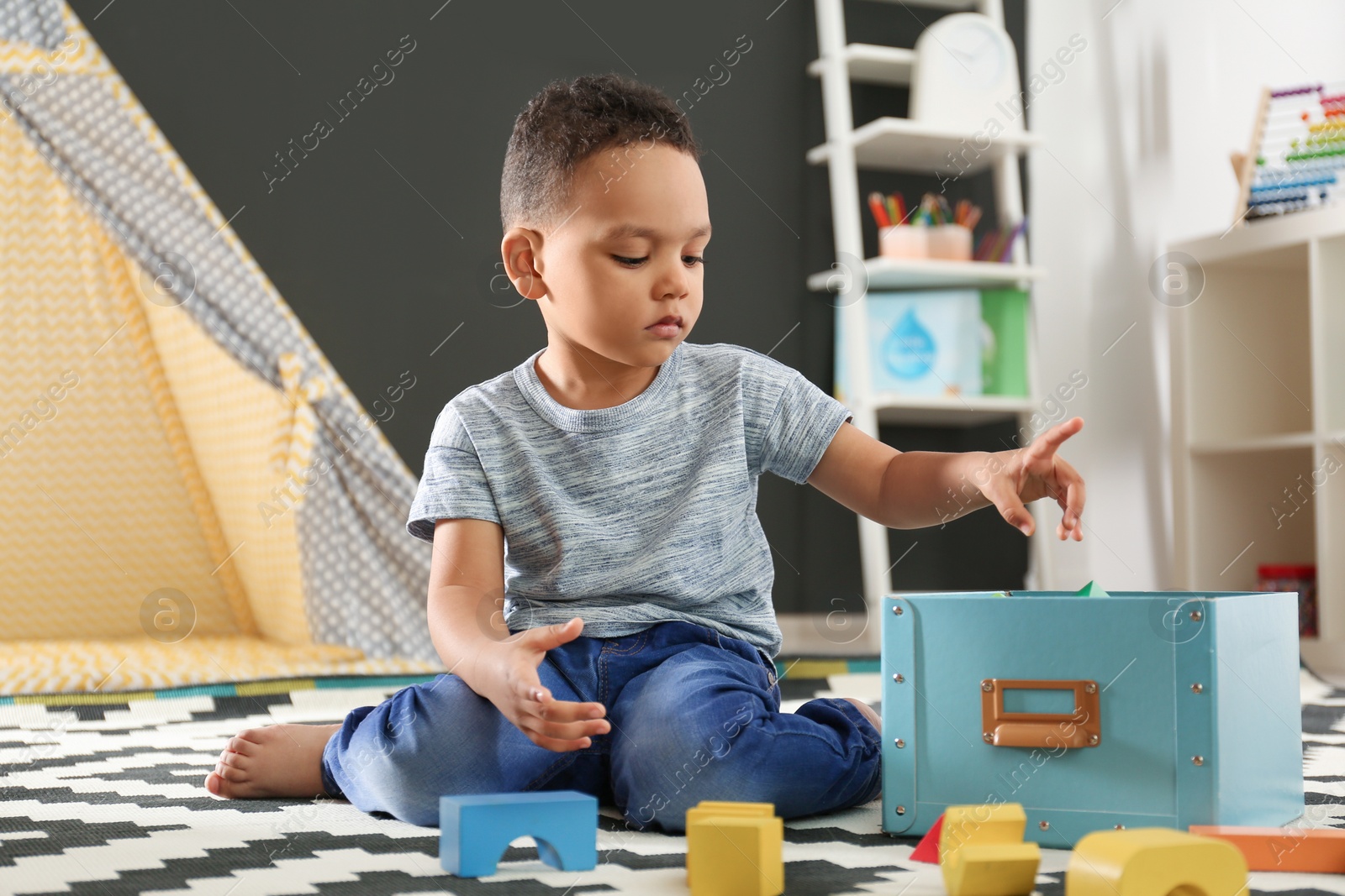 Photo of Cute little African-American child playing with building blocks on floor in kindergarten. Indoor activity