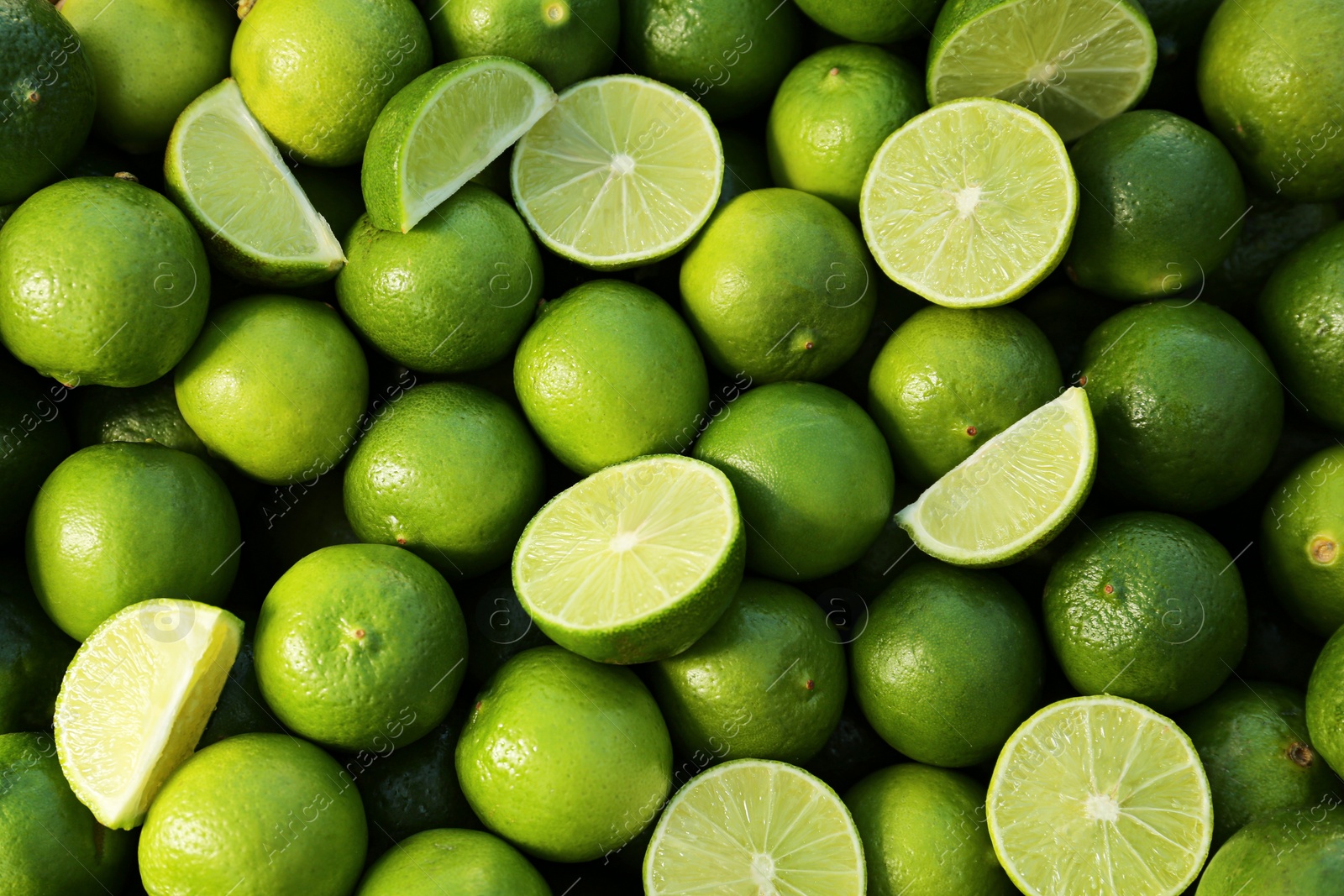 Photo of Whole and cut fresh ripe green limes as background, top view