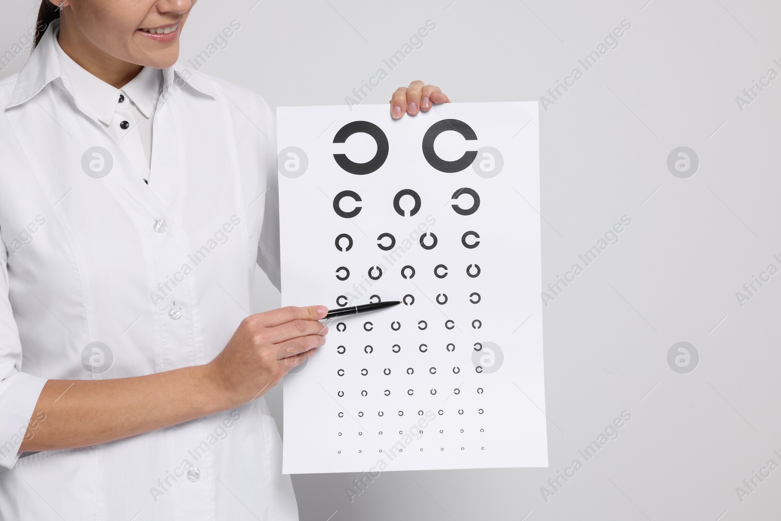 Photo of Ophthalmologist pointing at vision test chart on light background, closeup