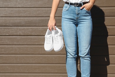 Photo of Woman holding stylish sneakers near wooden wall. Space for design