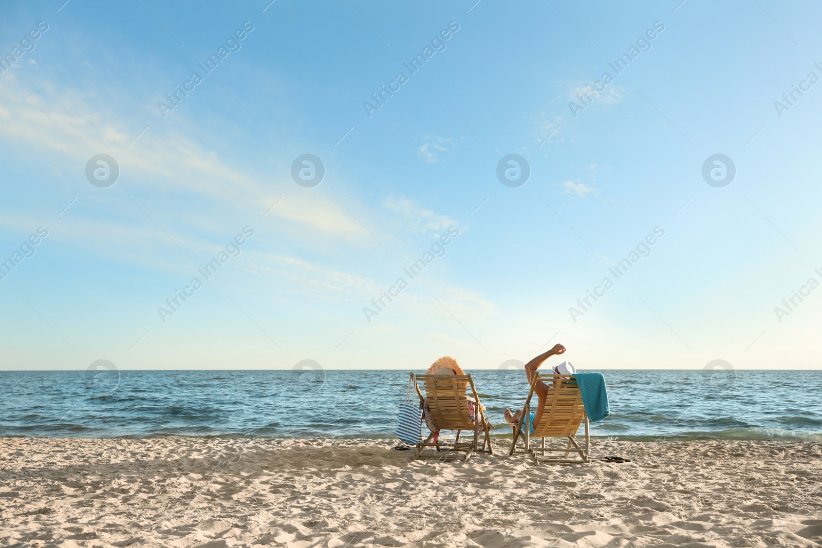 Photo of Young couple relaxing in deck chairs on beach near sea