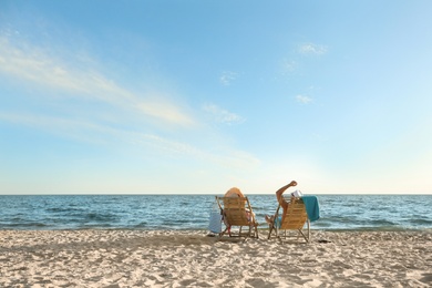 Young couple relaxing in deck chairs on beach near sea