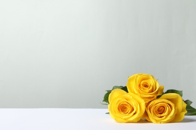Photo of Beautiful fresh yellow roses on white table against light grey background. Space for text