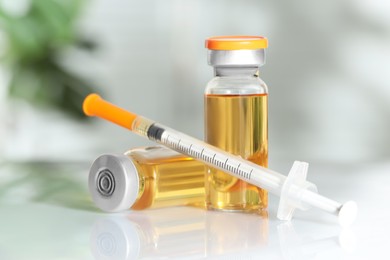 Photo of Glass vials and syringe with orange medication on white table, closeup