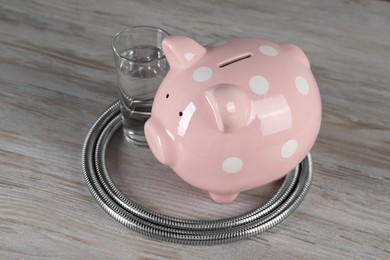 Photo of Water scarcity concept. Piggy bank, shower hose and glass of drink on wooden table