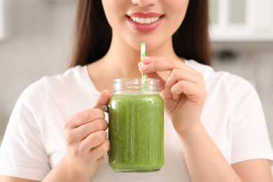 Woman holding delicious smoothie indoors, closeup view