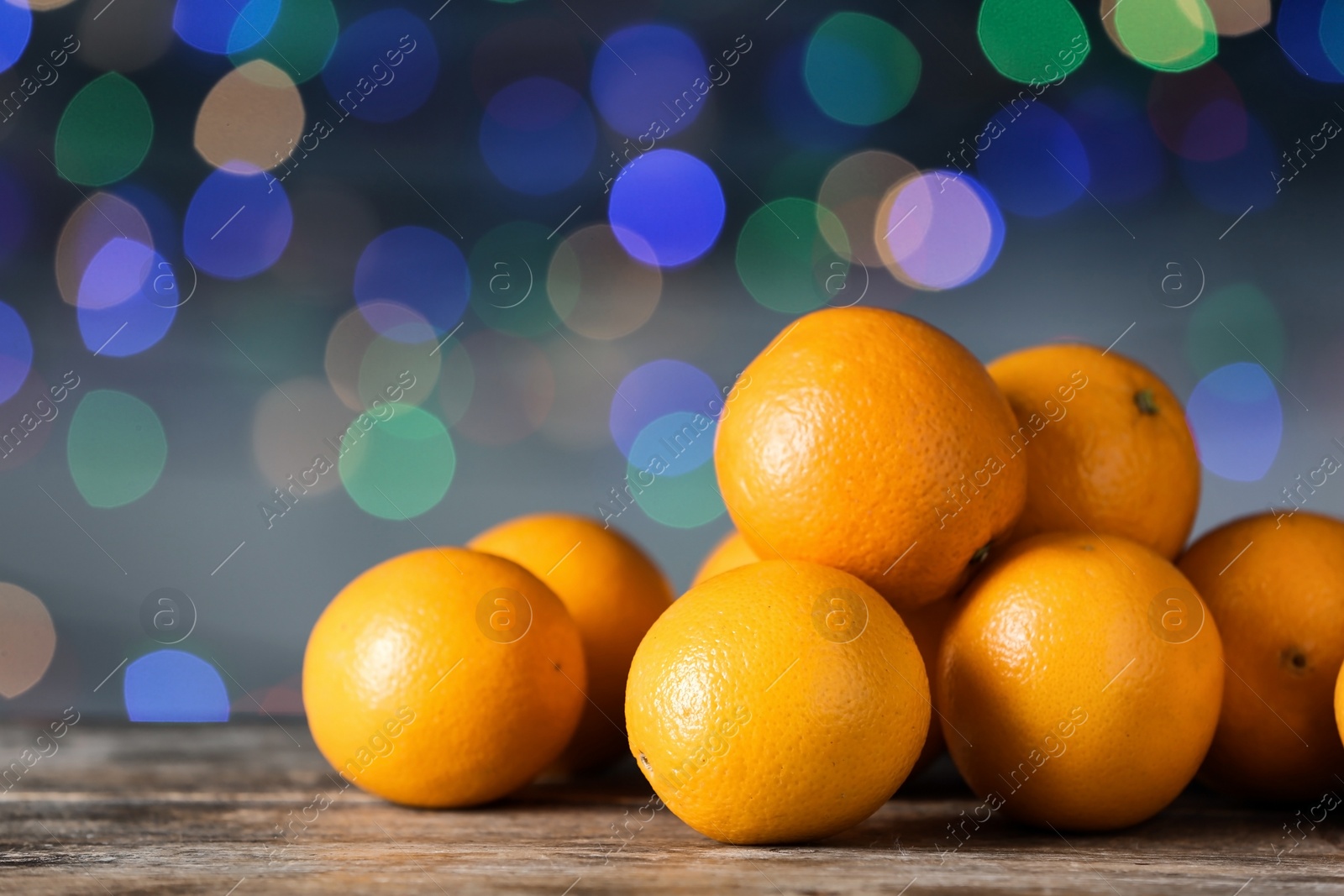 Photo of Fresh oranges on wooden table against blurred lights. Bokeh effect