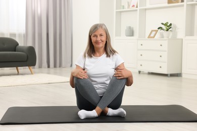 Happy senior woman sitting on mat at home. Yoga practice