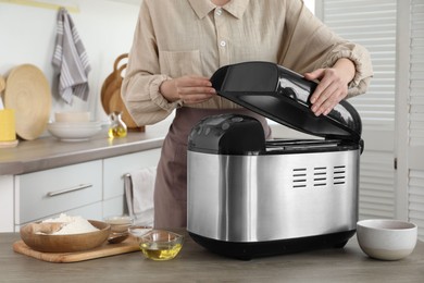 Photo of Woman using breadmaker machine at wooden table in kitchen, closeup