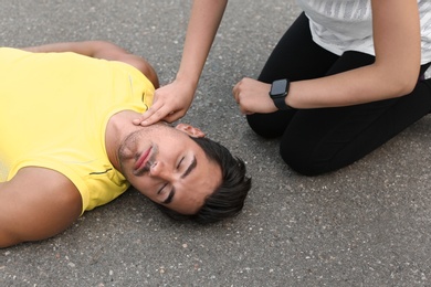 Photo of Young woman checking pulse of unconscious man on street