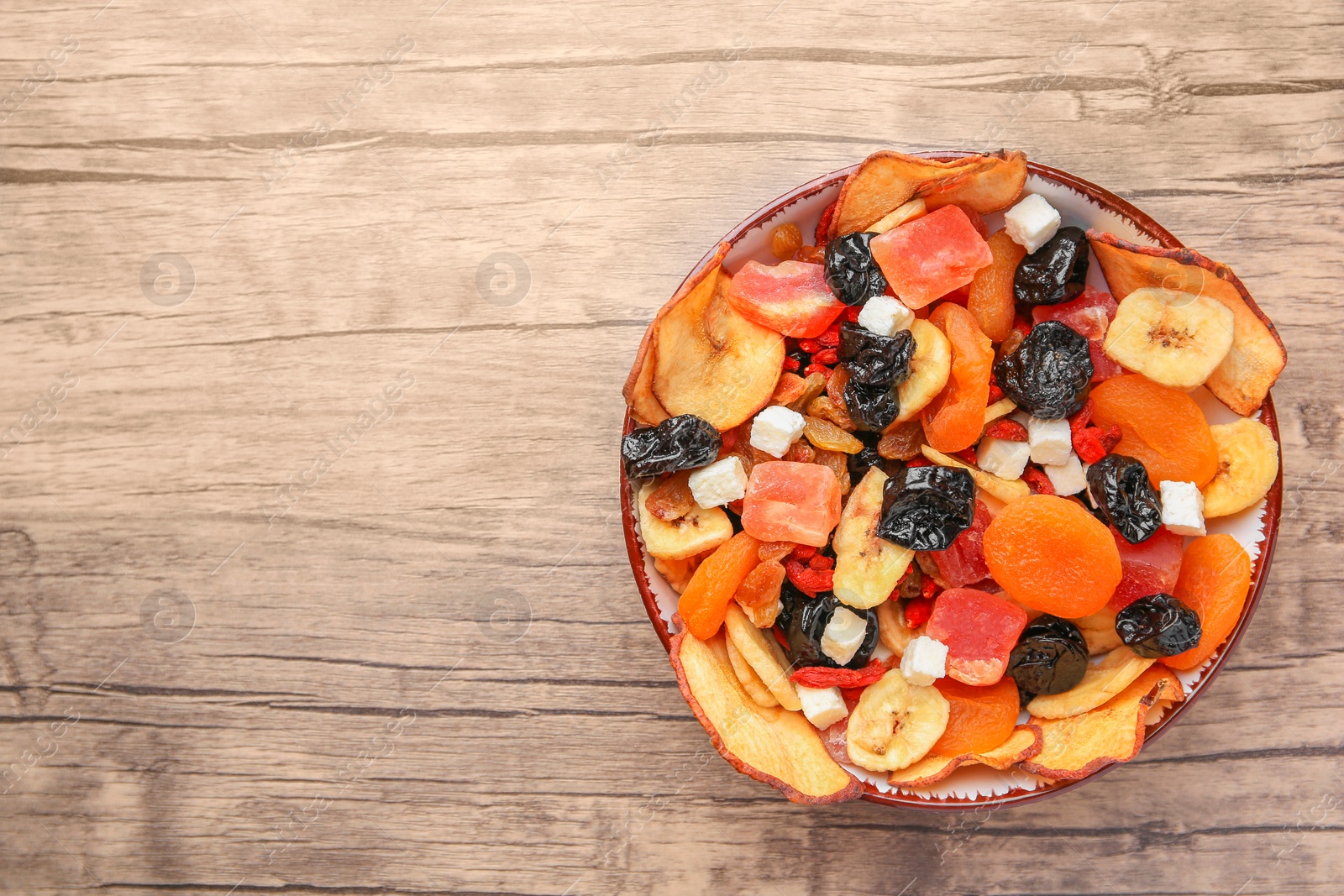 Photo of Bowl with different tasty dried fruits on wooden table, top view. Space for text