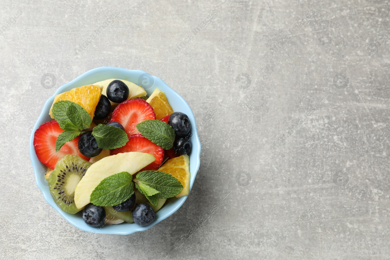 Photo of Tasty fruit salad in bowl on gray textured table, top view. Space for text