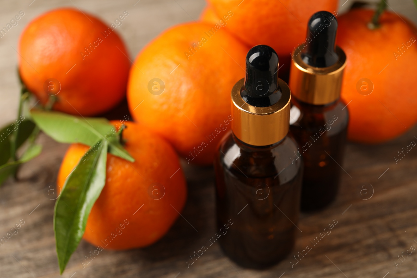 Photo of Bottles of tangerine essential oil and fresh fruits on wooden table, closeup