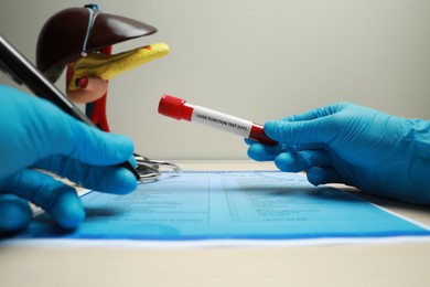 Photo of Liver Function Test. Laboratory worker with tube of blood sample filling in form at table, closeup