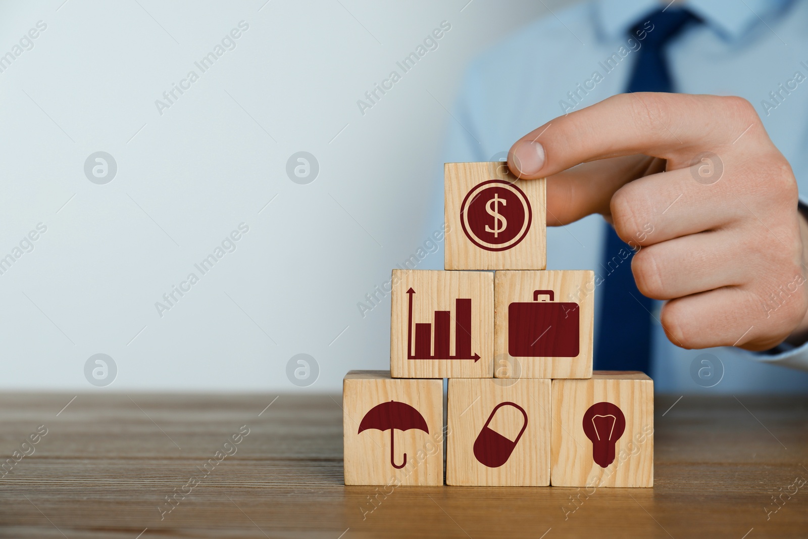 Image of Man building pyramid of cubes with different icons at wooden table, closeup. Insurance concept