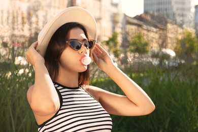 Beautiful woman in stylish sunglasses blowing gum outdoors on sunny day