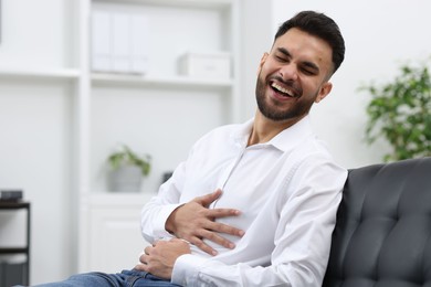 Photo of Handsome young man laughing on sofa in office