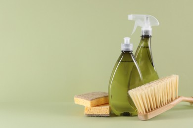 Bottles of cleaning product, sponges and brush on light green background. Space for text