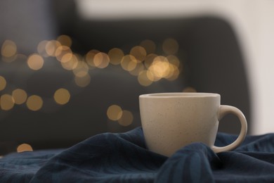 Photo of Cup of drink on soft knitted blanket against blurred lights. Space for text