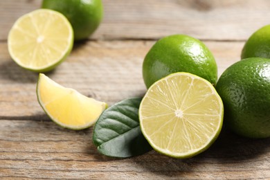 Whole and cut fresh limes on wooden table, closeup