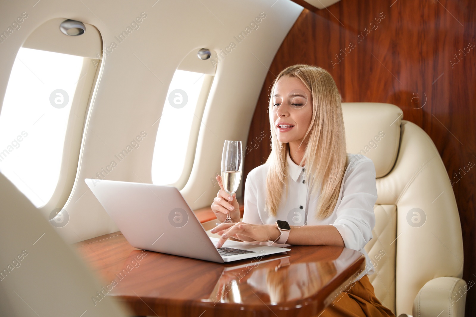 Image of Happy woman with glass of champagne working on laptop during flight