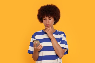Photo of Thoughtful young woman with smartphone on orange background