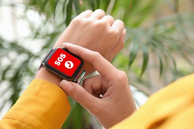 Woman using SOS function on smartwatch indoors, closeup