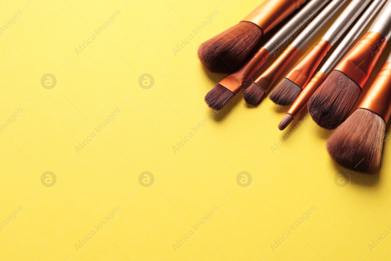 Photo of Different makeup brushes on yellow background. Space for text
