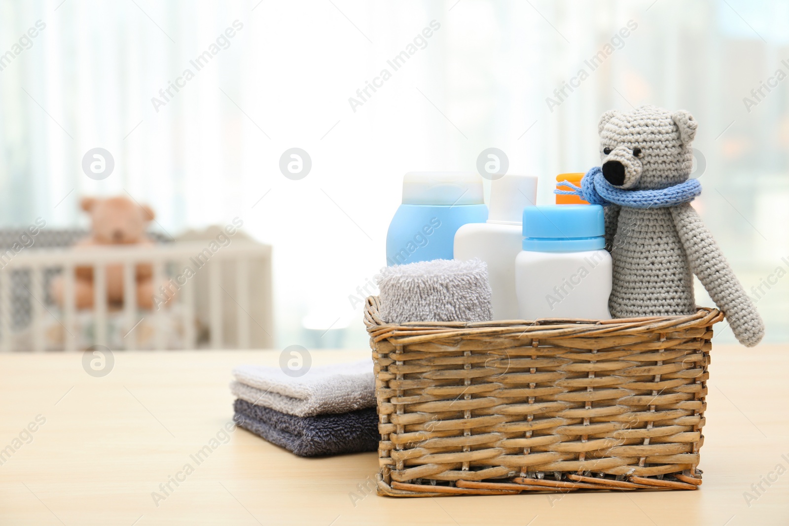 Photo of Wicker basket with baby cosmetic products, toy and towels on table indoors. Space for text