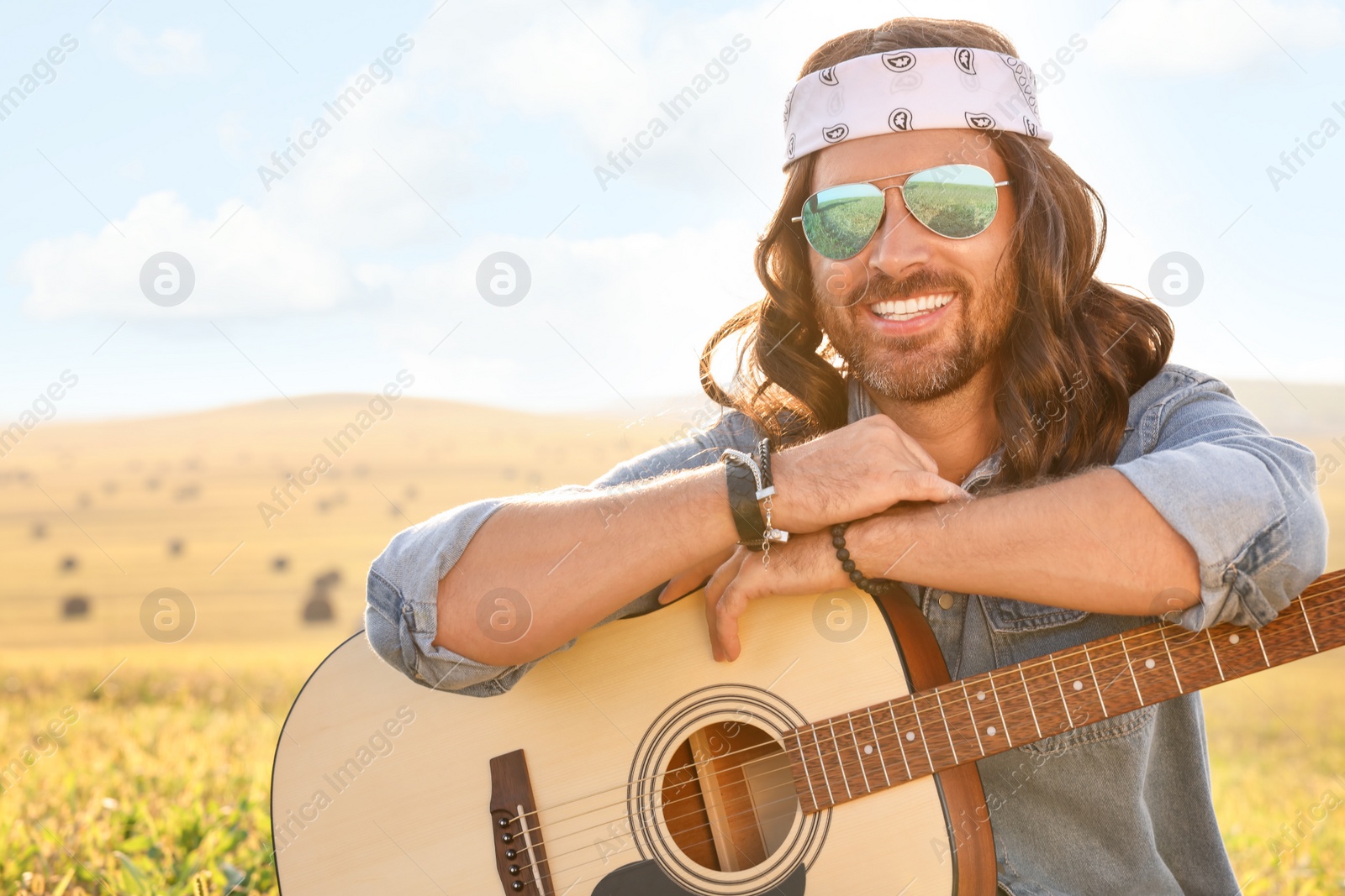 Photo of Portrait of happy hippie man with guitar in field