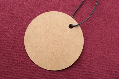 Photo of Circle shaped tag with space for text on dark red fabric, top view