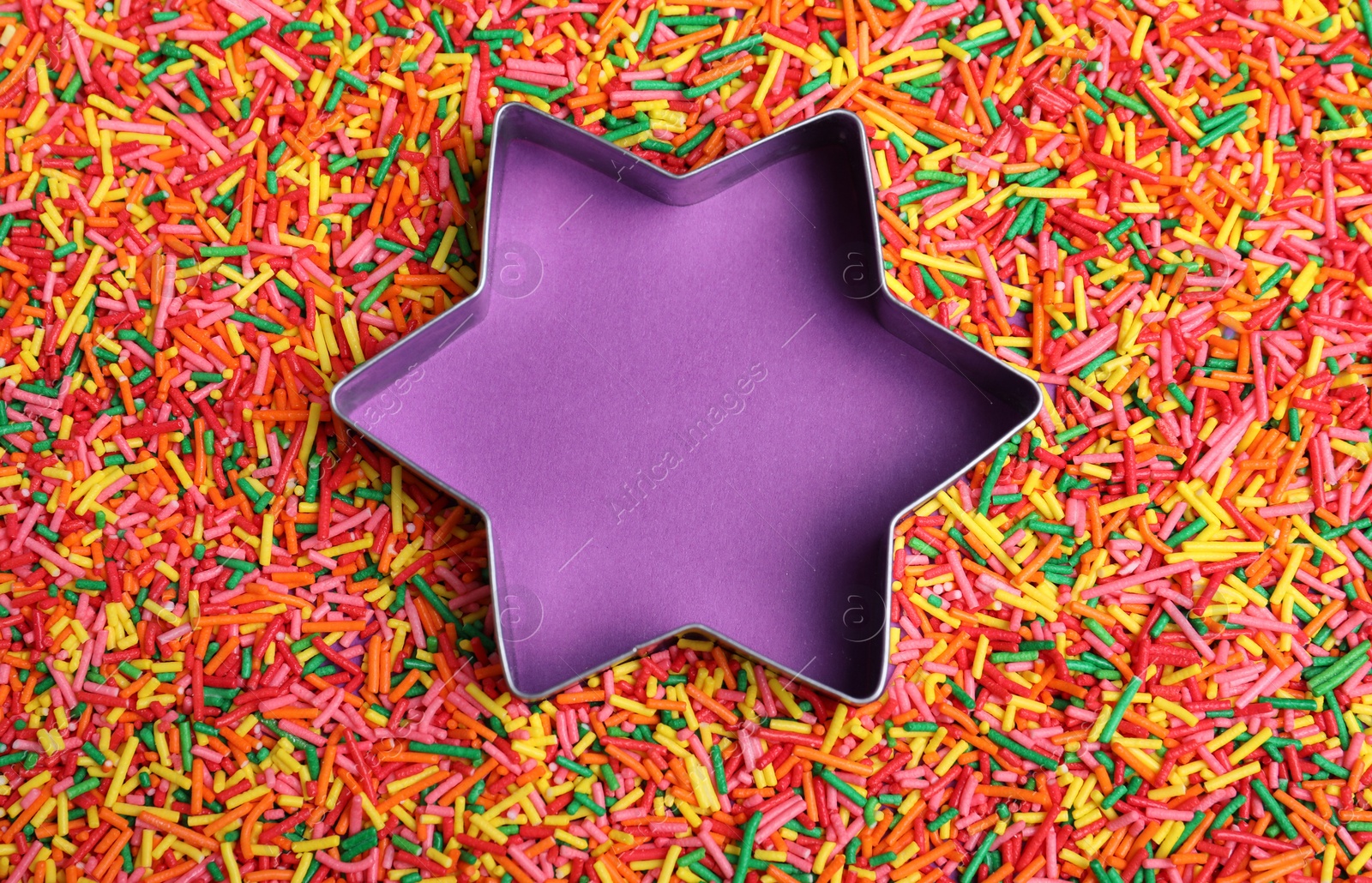 Photo of Star shaped cookie cutter and sprinkles on purple background, flat lay with space for text. Confectionery decor