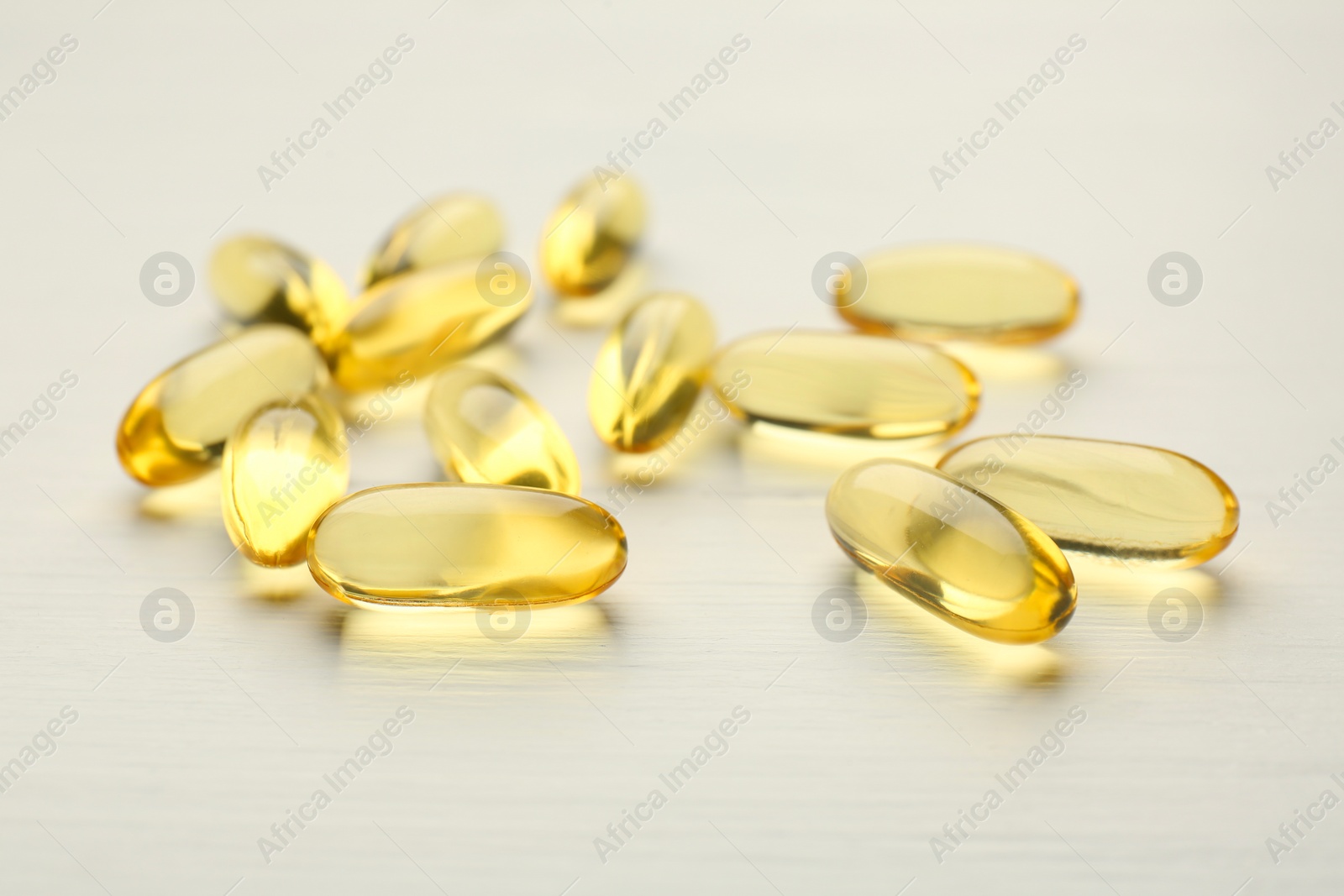 Photo of Yellow vitamin capsules on white wooden table, closeup